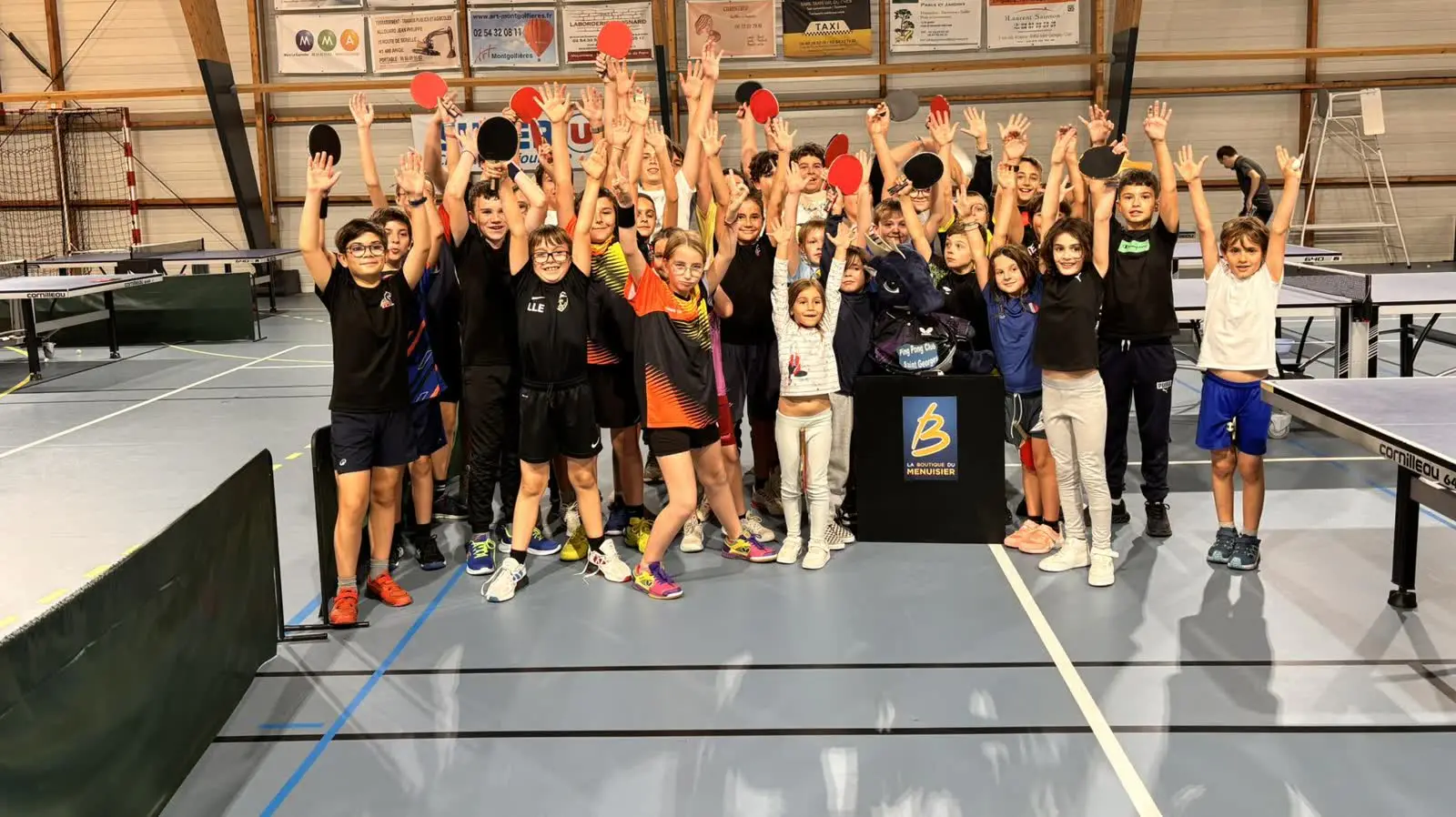 Un groupe de jeunes du club, filles et garçons, bras levés et raquettes à la main dans la salle Omnisport.